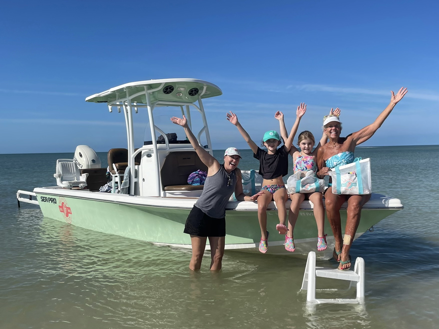 Four people posing on a boat in shallow water under a clear blue sky.