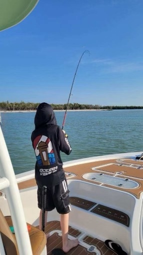 Person fishing from a boat under clear blue skies.