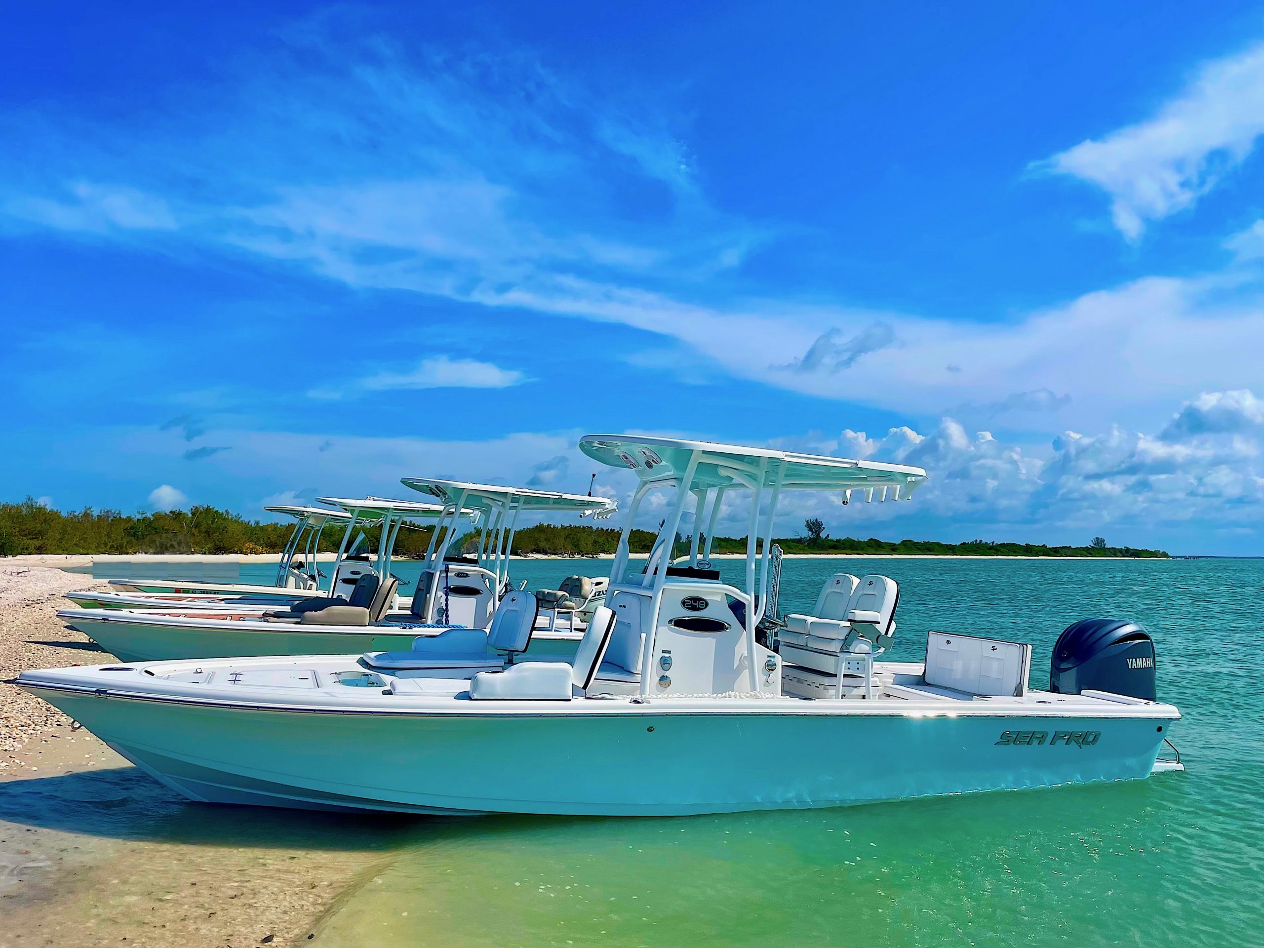 Four white boats docked on a sandy beach under a blue sky.