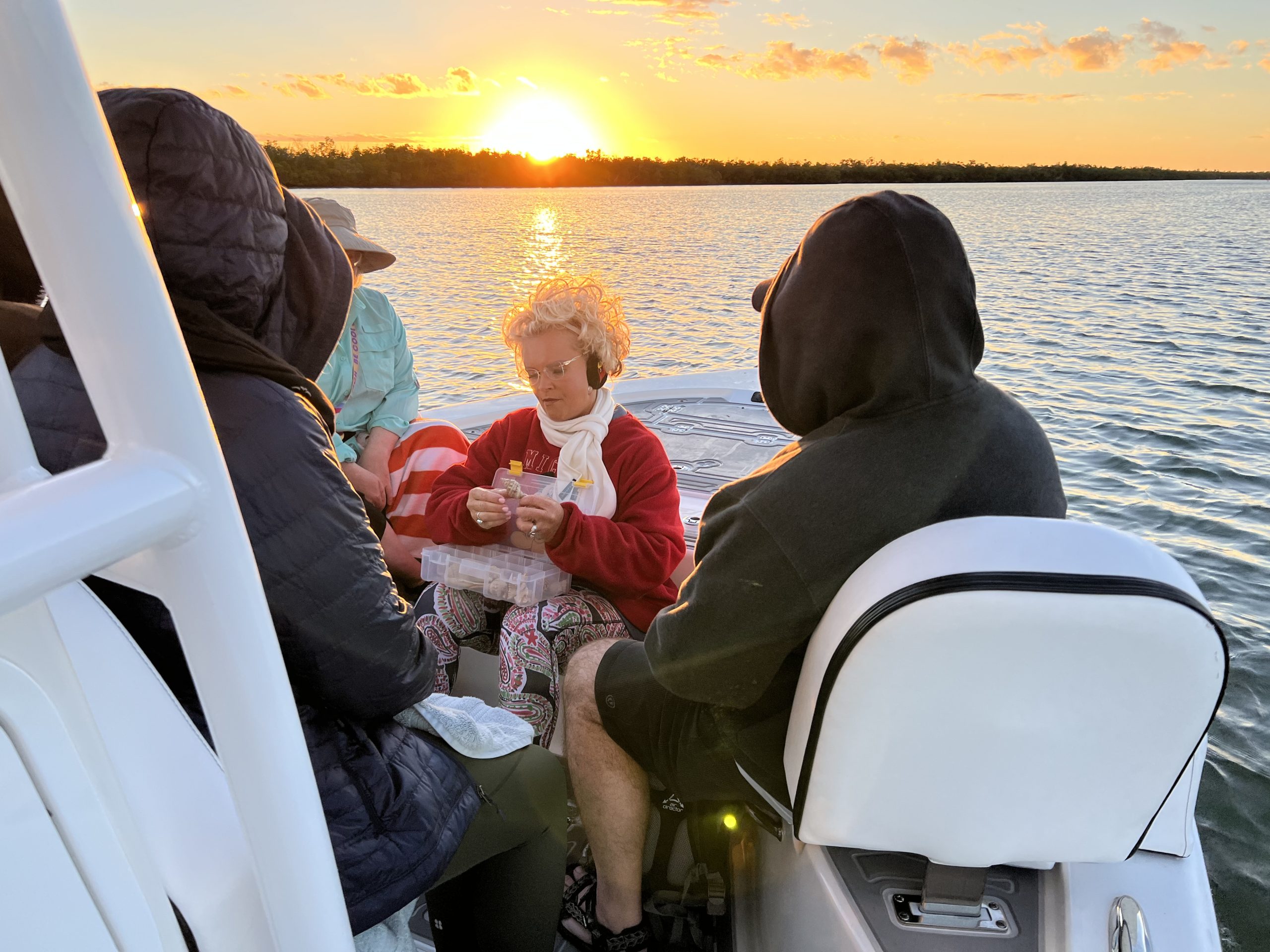 People on a boat at sunset, sitting and talking, with water visible.