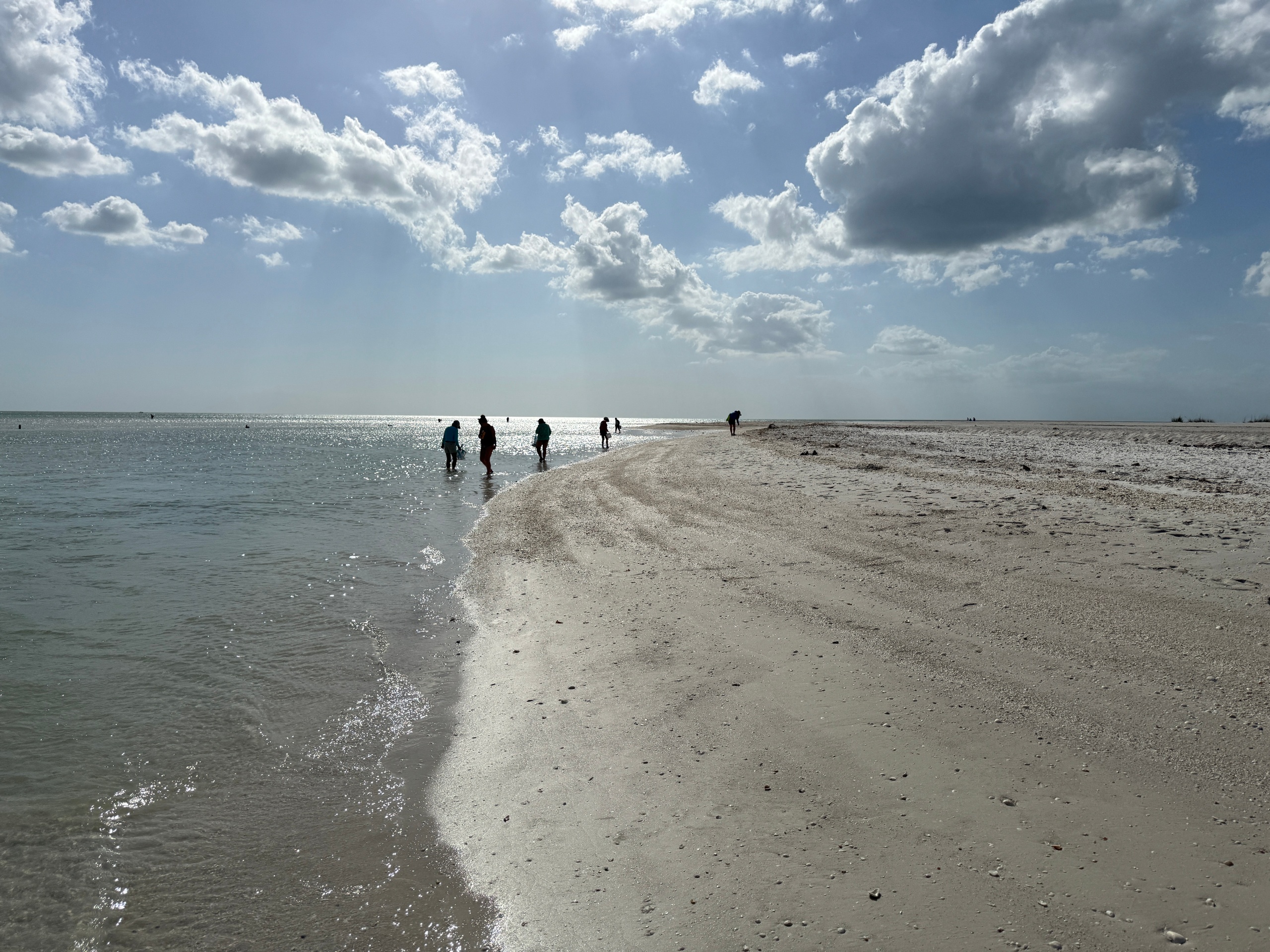 People walking on a sandy beach under a cloudy sky.