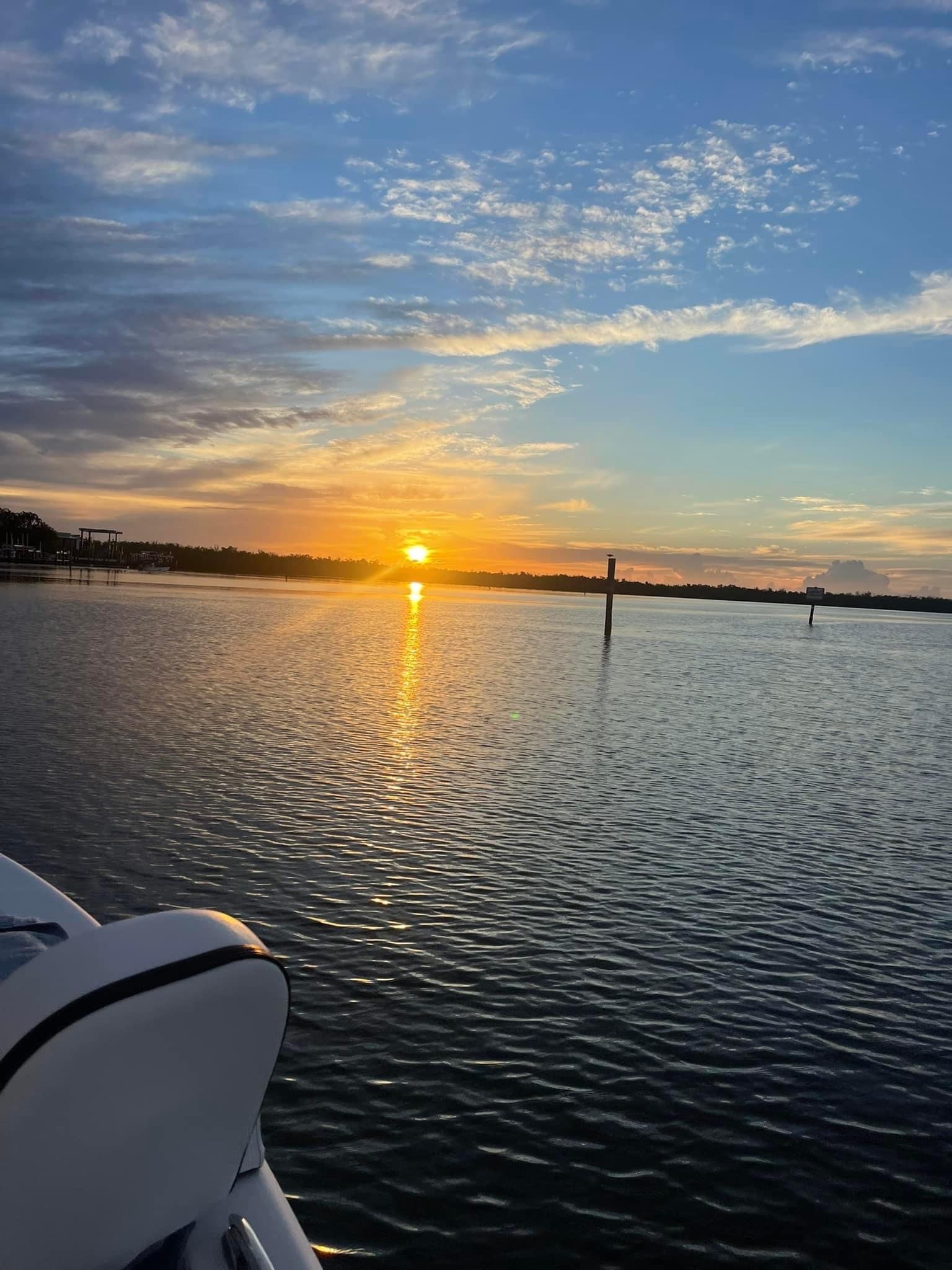 Sunset over a calm lake with reflections and scattered clouds in the sky.