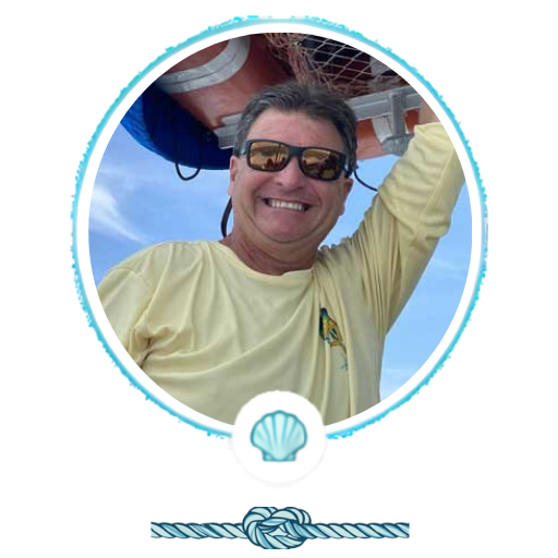 Man in yellow shirt and sunglasses smiles on a boat, with a life preserver in the background.