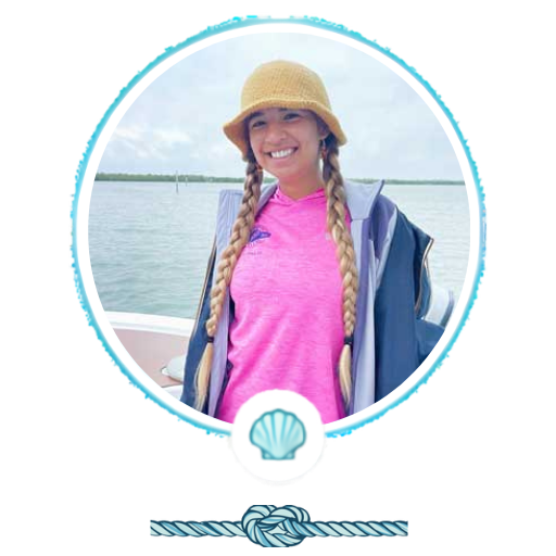 Person in a pink shirt and hat smiling on a boat with water and trees in the background.