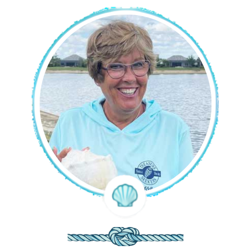 Smiling person in glasses by a lake, wearing a light blue hoodie.