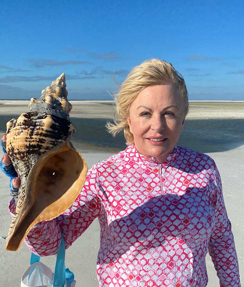 Person holding large seashell on a sunny beach.