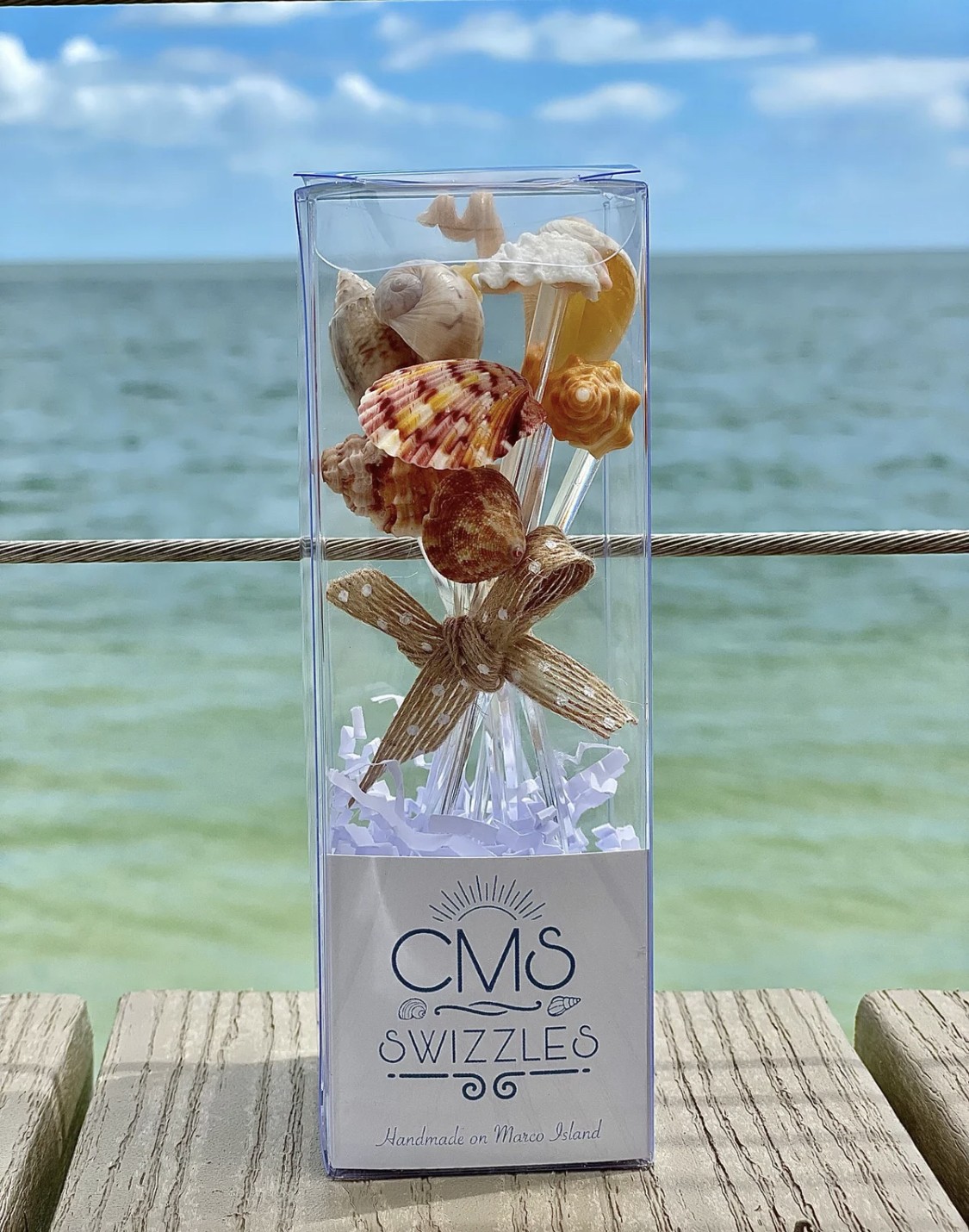 Box of seashell swizzles with ocean background.