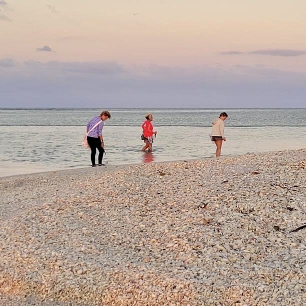 Three people walking along a pebbly beach at sunset.