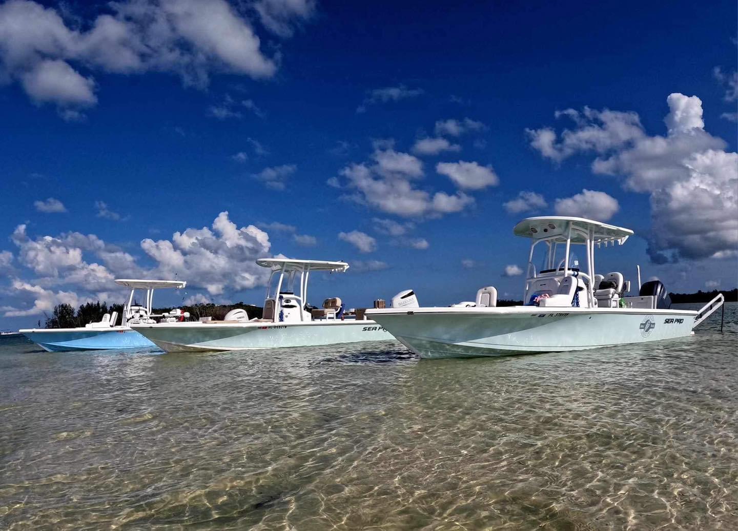 Three motorboats anchored in clear shallow water under a partly cloudy sky.