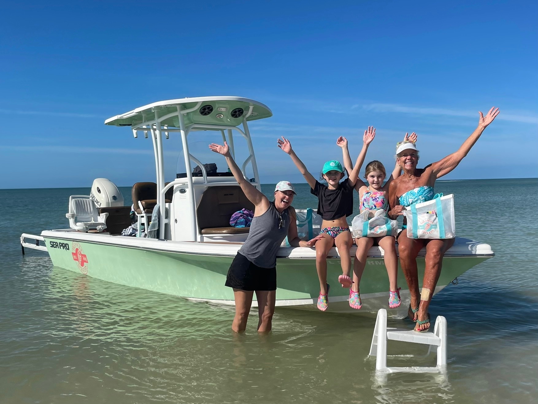 Four people smiling on a boat in shallow water, with arms raised.