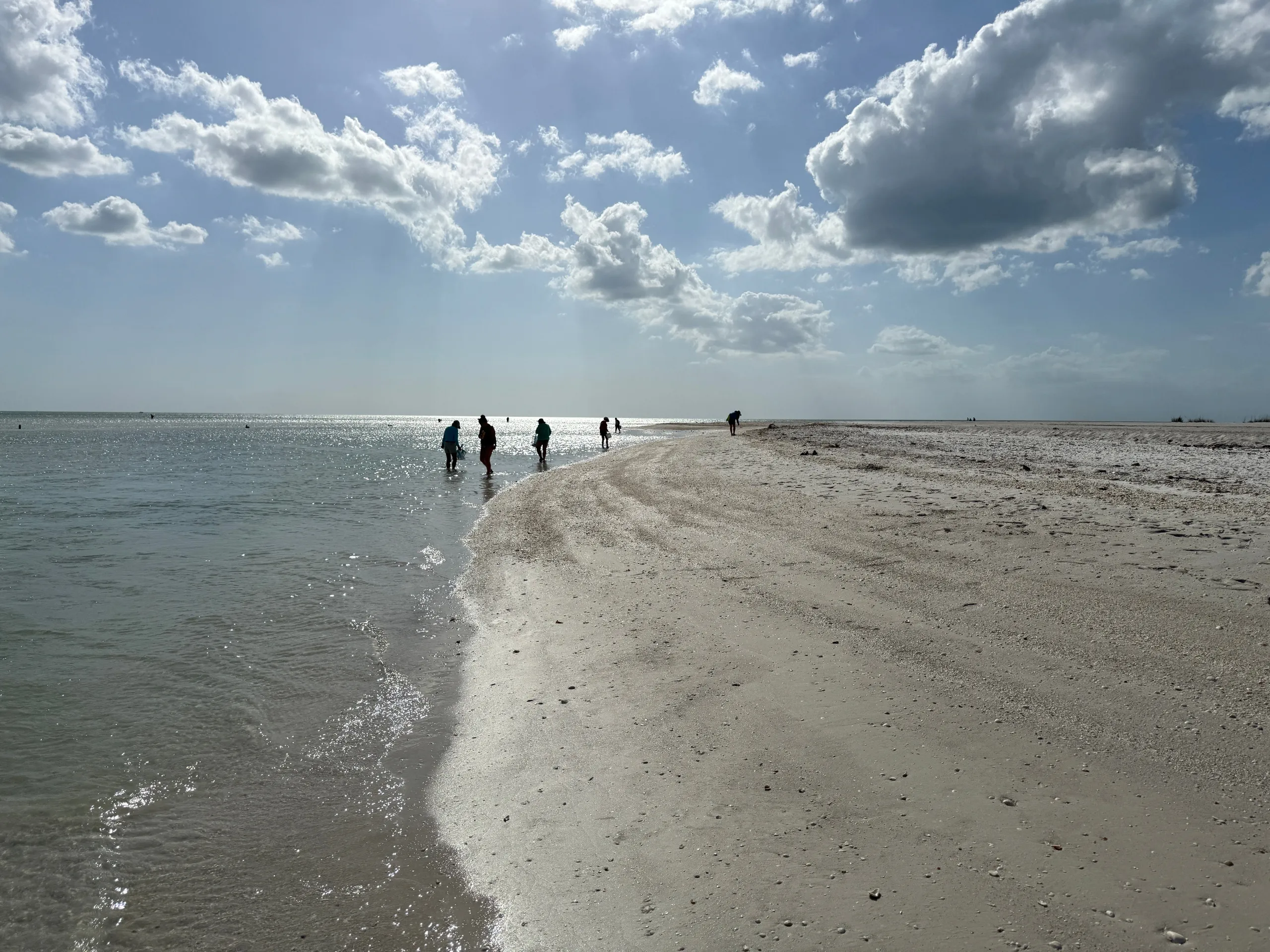 People walking on a sandy beach under a cloudy sky.