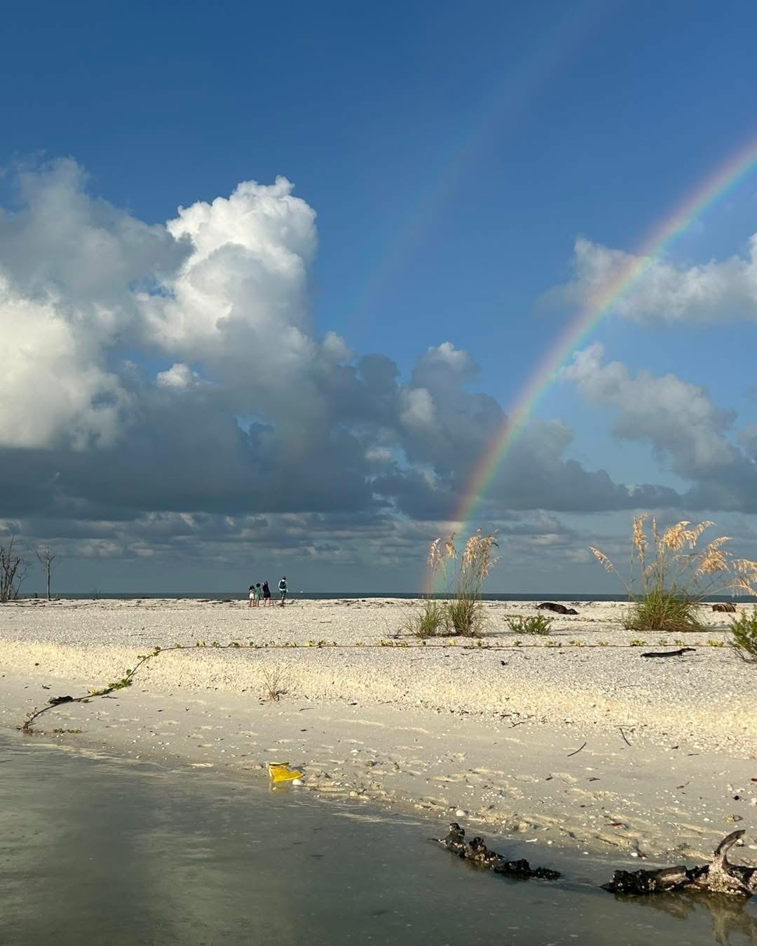 Beach scene with double rainbow and cloudy sky