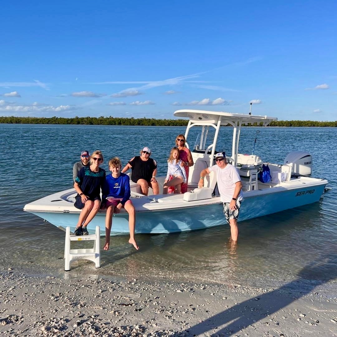 Six people on a boat at the shoreline under a clear blue sky.
